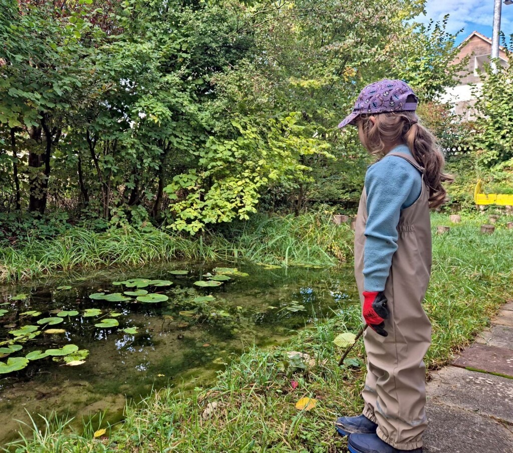 Mädchen steht an einem kleinen Teich und beobachtet Wasserläufer